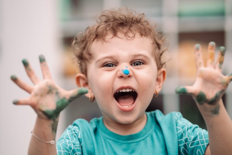 Criança sorrindo com as mãos sujas de tinta verde em atividade de artes