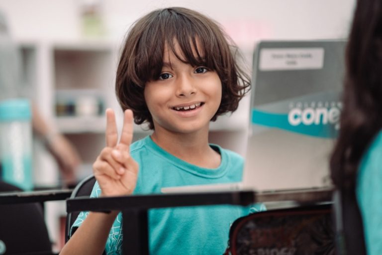 Aluno sorrindo e fazendo sinal de paz na sala de aula
